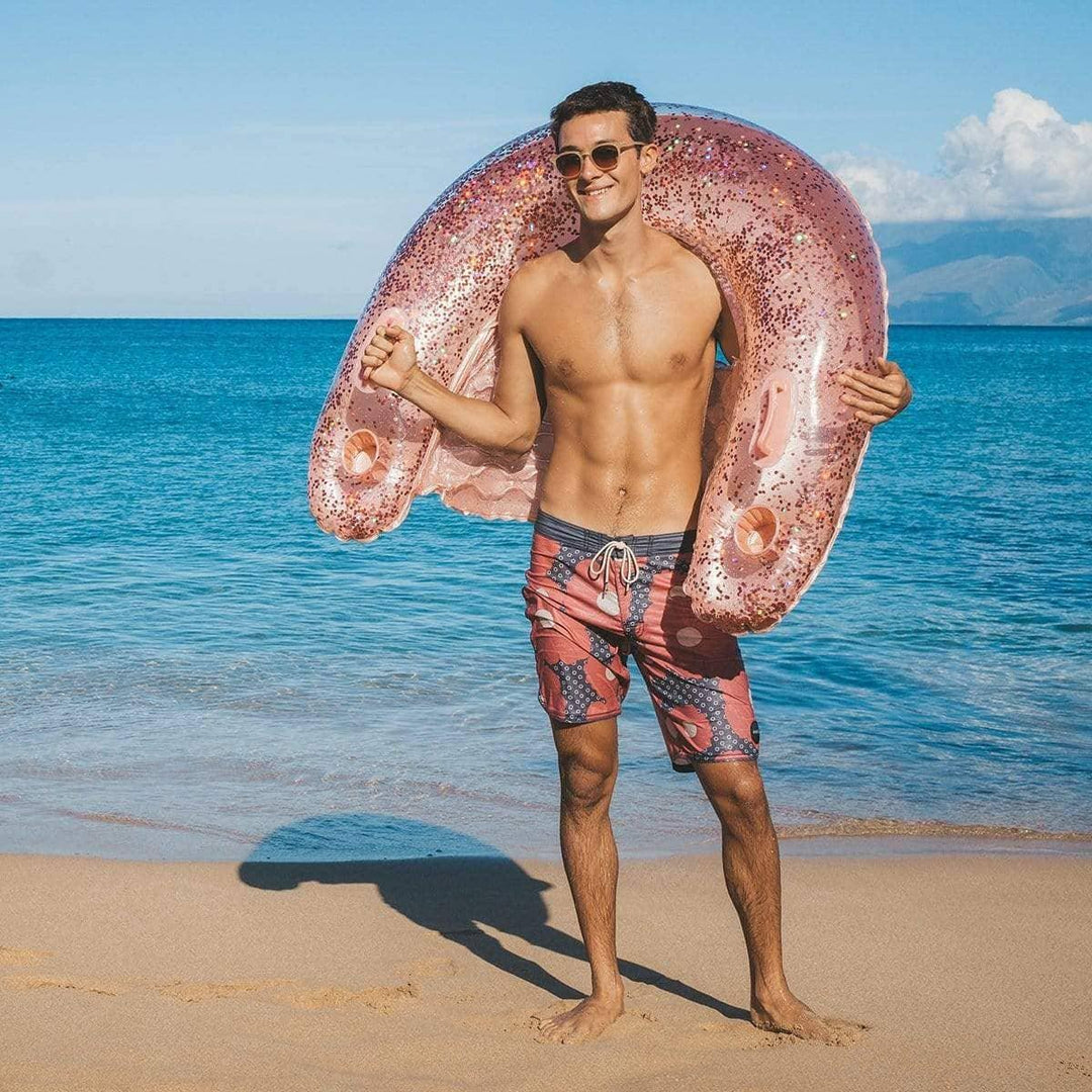 Man on beach holding pink glitter inflatable ring, ready for ocean fun and summer adventures.