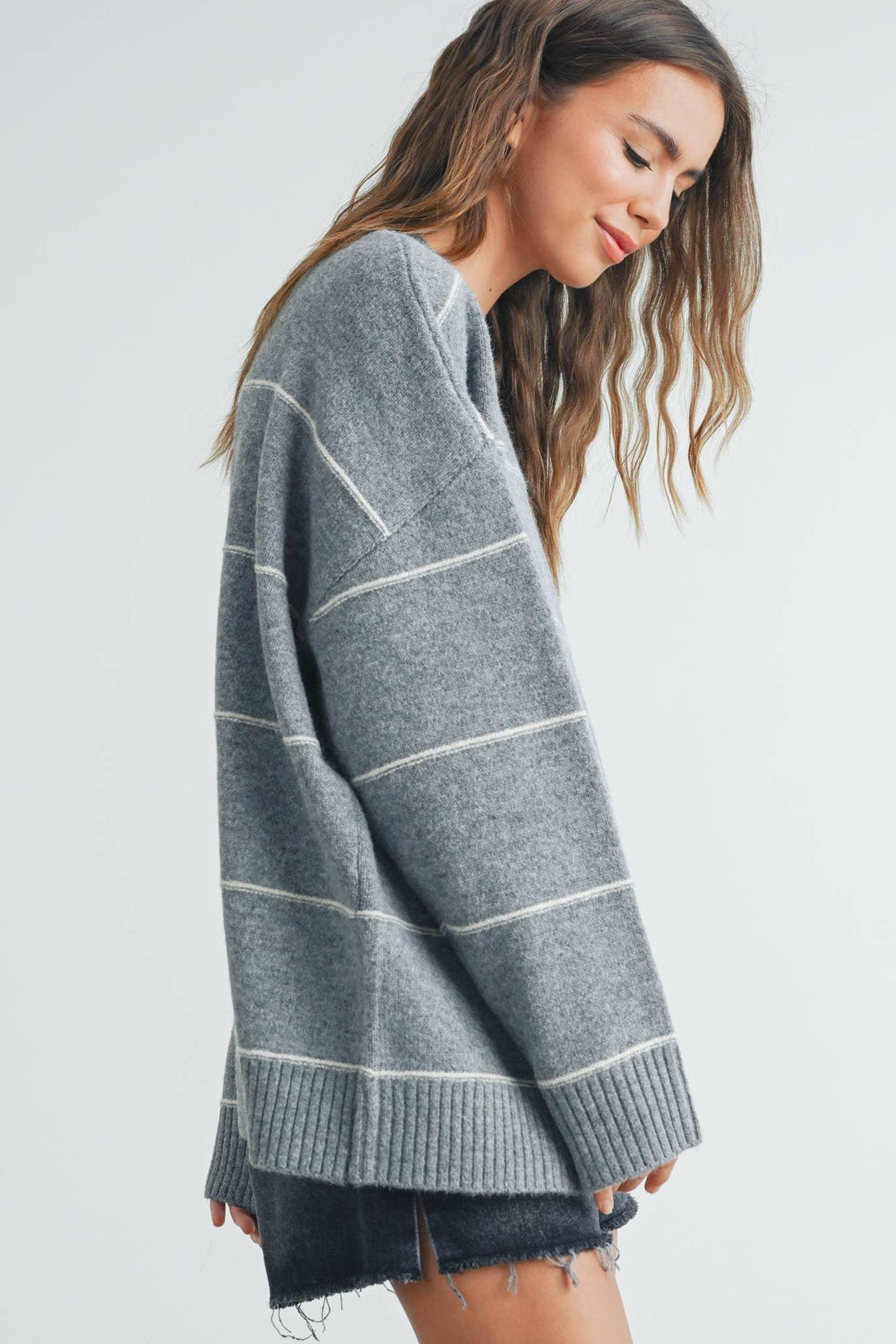 Woman wearing cozy gray striped oversized sweater with ribbed hem, paired with denim shorts