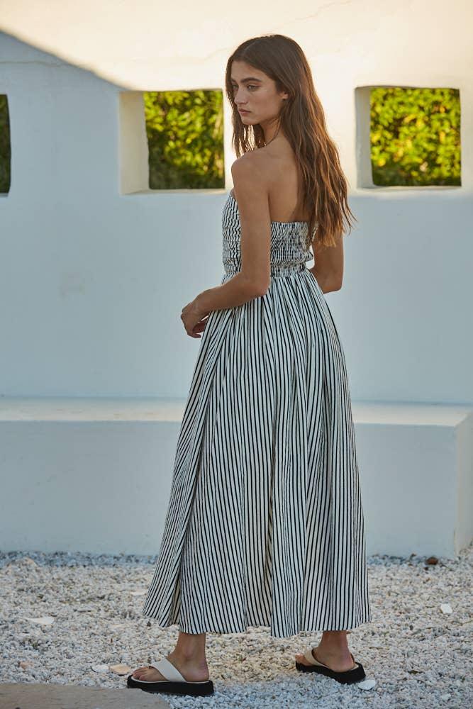 Woman in black and white striped strapless maxi dress, coastal outdoor setting, beach style