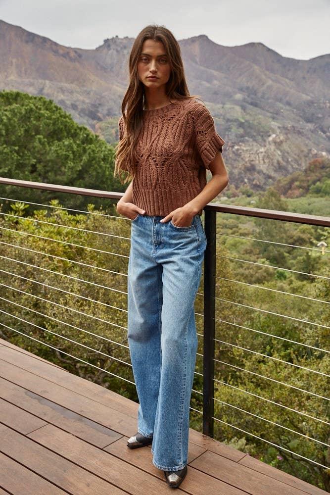 Woman in cozy brown knit top and wide-leg jeans on mountain deck, PNW outdoor style