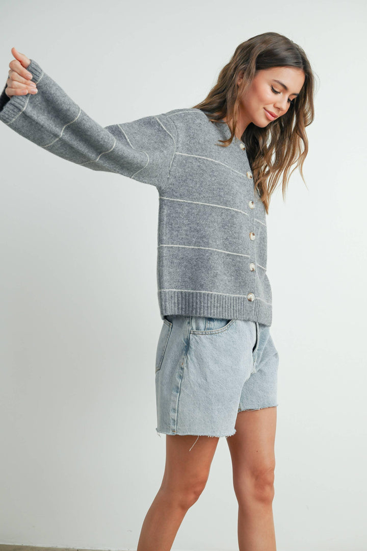 Woman in gray striped button-up cardigan and light denim shorts, coastal style outfit