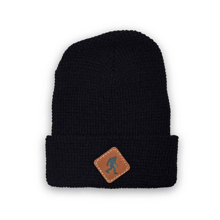 Black knit beanie with brown leather patch featuring a Bigfoot silhouette, perfect for PNW outdoor adventures.