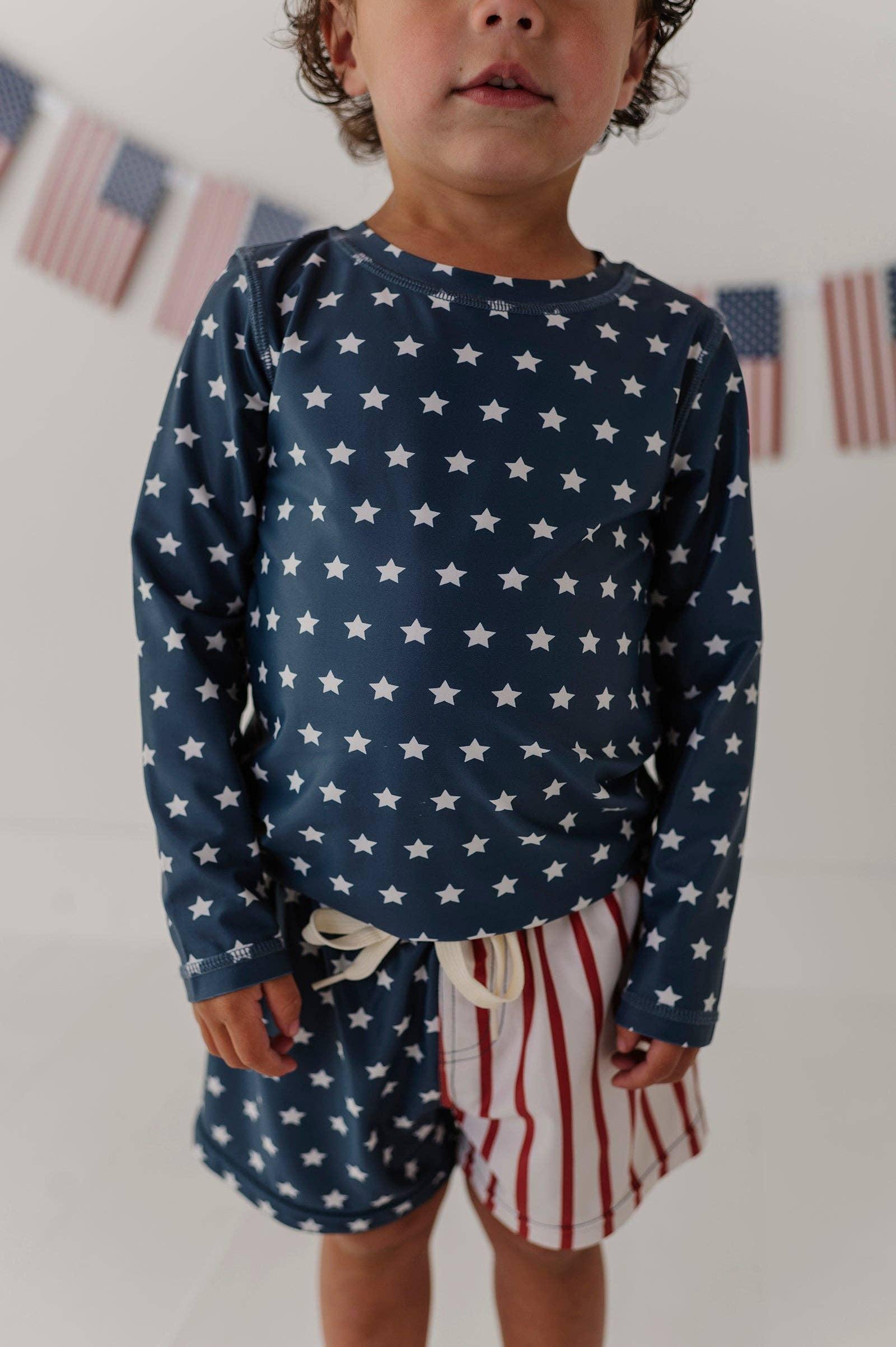 Toddler in navy star print long sleeve rash guard and red white striped swim trunks