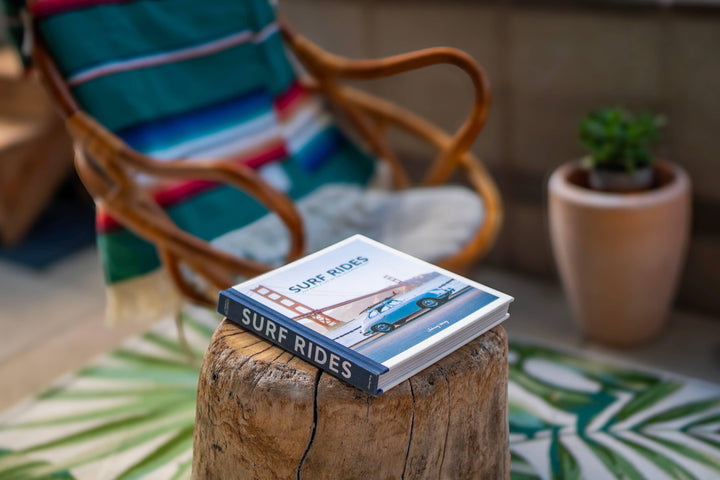 Surf Rides book on wooden stump with striped chair and palm rug, coastal lifestyle decor