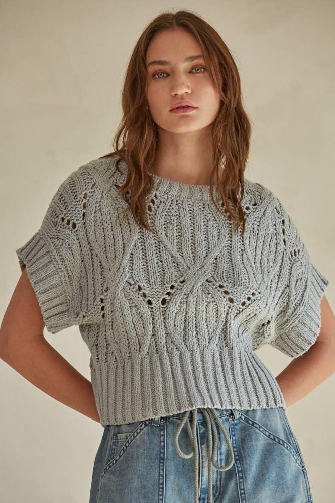 Gray knitted crop top with cable knit and lace details, paired with denim shorts