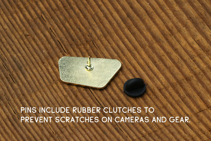 Back view of a Squatchy enamel pin showing the gold post and black rubber clutch on wood.