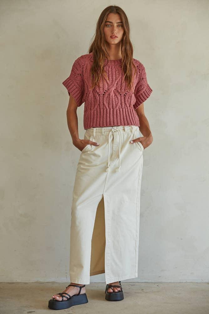 Woman in pink cable knit crop top and cream wide-leg pants with front slit, styled with black platform sandals