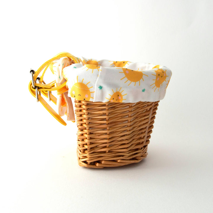 Woven bike basket with cheerful sun-patterned liner and yellow straps, perfect for coastal adventures.