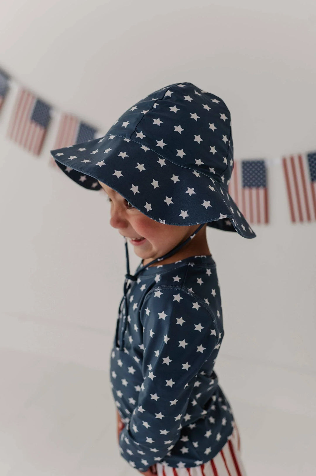 Toddler in navy star-print sun hat and matching rash guard, perfect for beach days and outdoor adventures.
