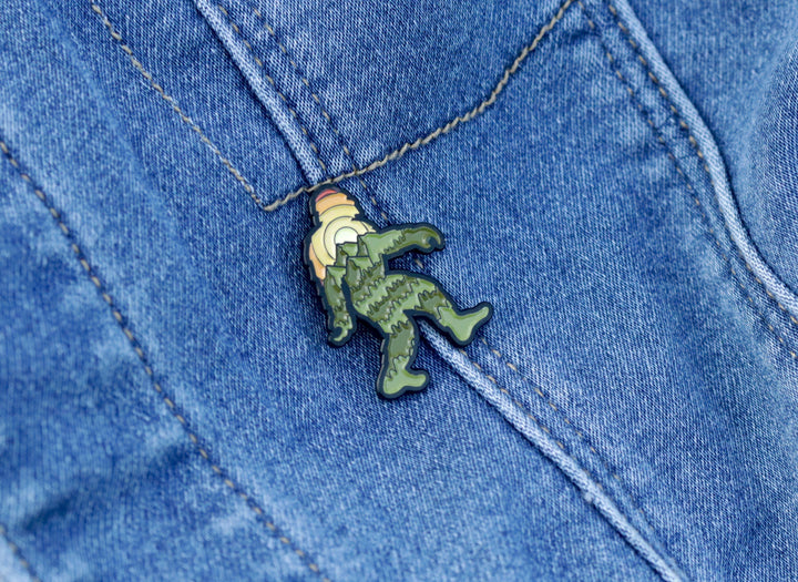 Green enamel pin of a hiking figure on denim fabric, ideal for outdoor enthusiasts.