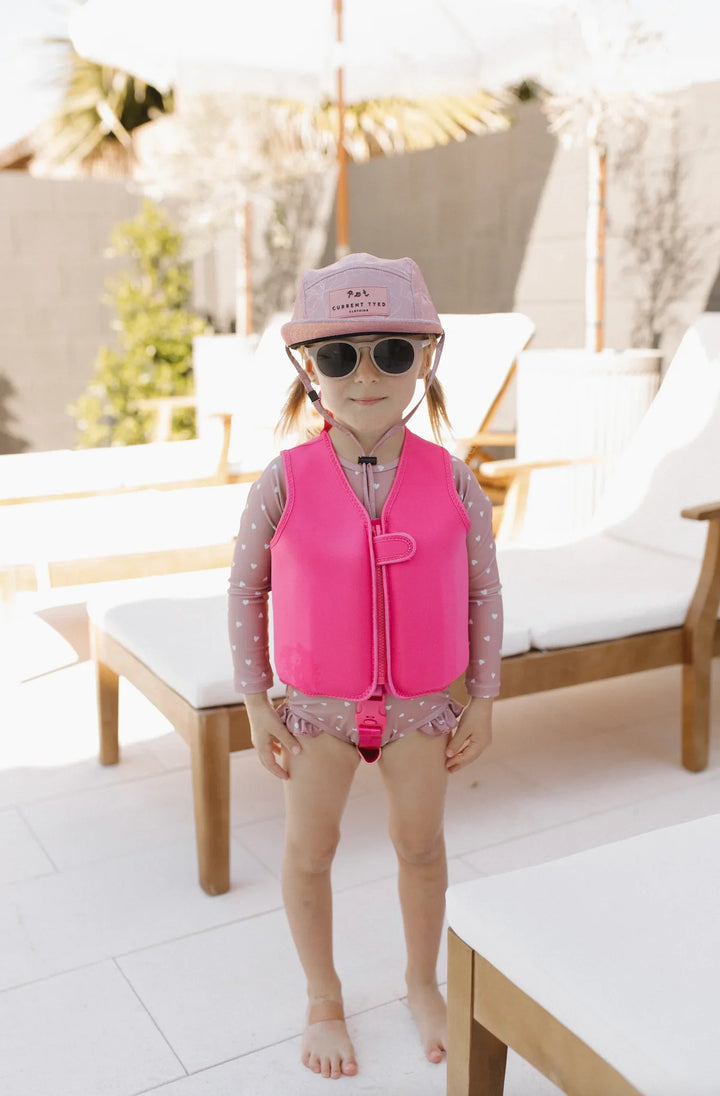 Child in pink life vest and sun hat by poolside lounge chairs