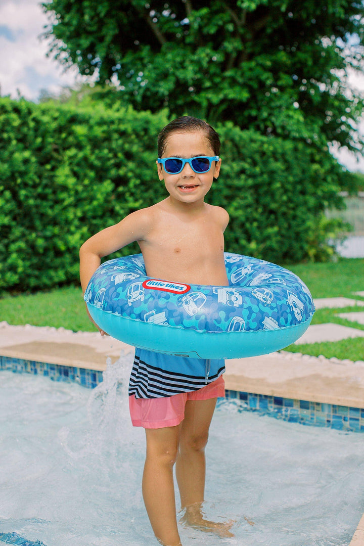 Child wearing sunglasses holding blue inflatable swim ring by pool