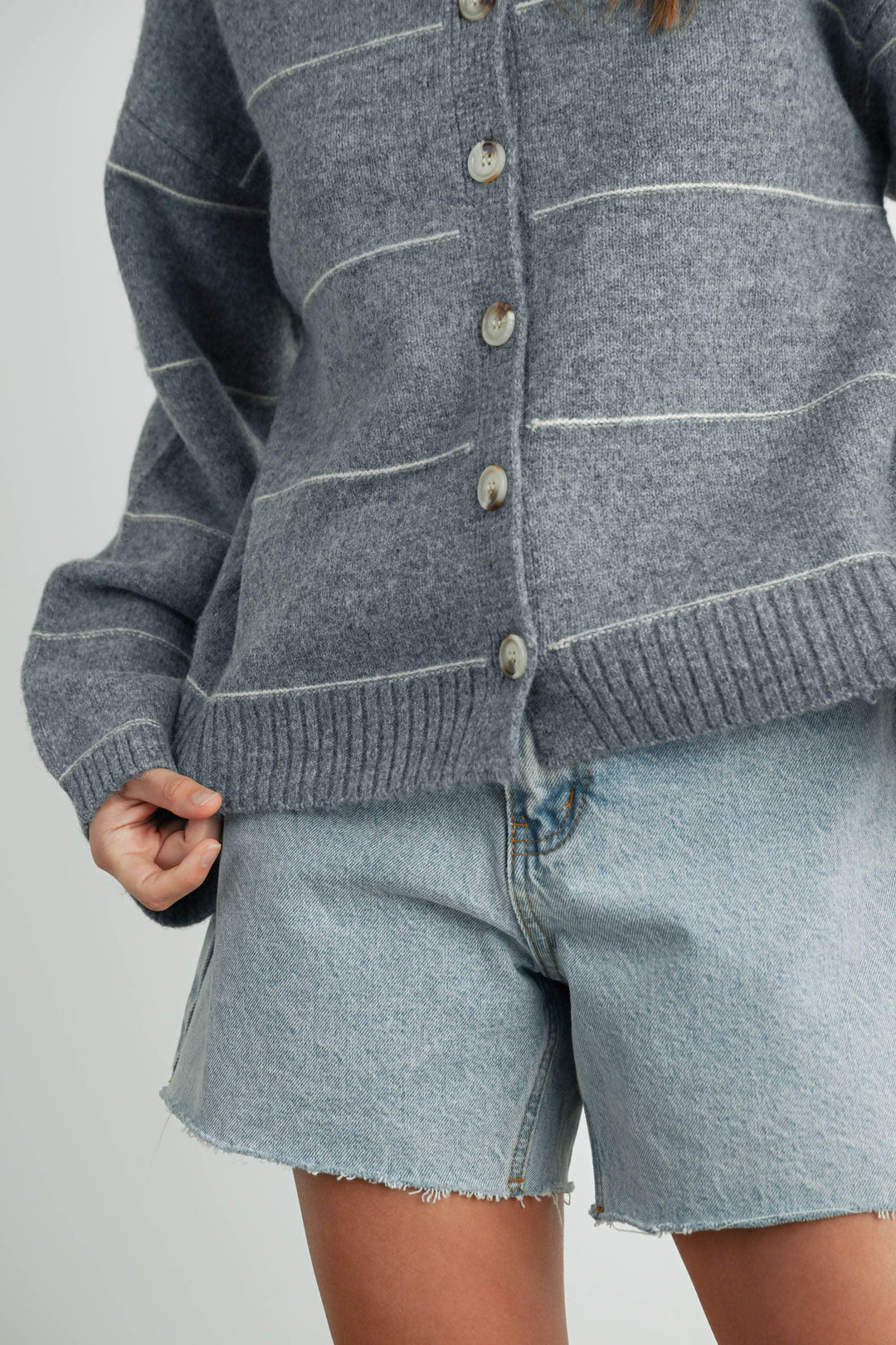 Cozy gray knit cardigan with cream stripes and buttons, paired with light denim shorts for casual coastal style.