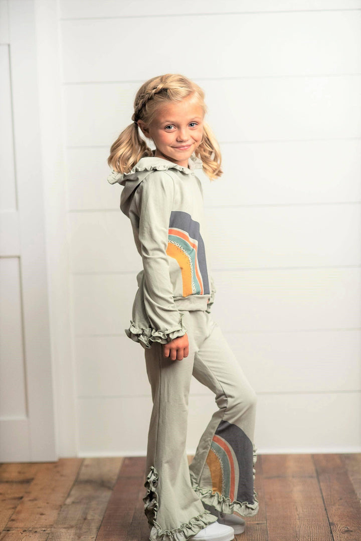 Girl wearing Oopsie Daisy gray sage rainbow hooded sweatsuit lounge set with ruffle trim.