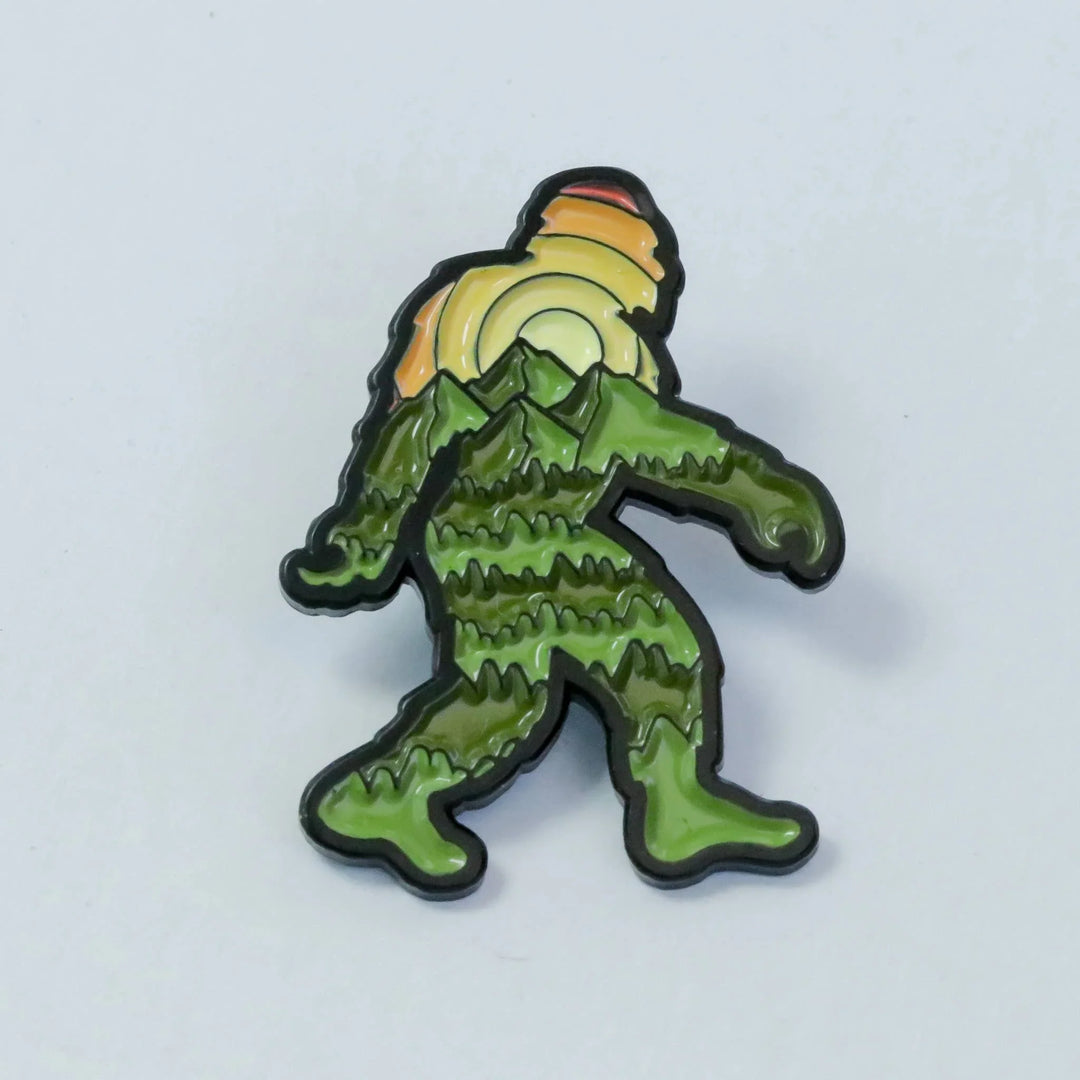 Green Bigfoot enamel pin with mountain and sunset design