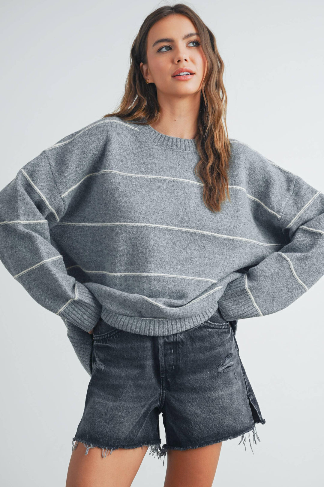 Woman in gray striped oversized sweater and distressed denim shorts