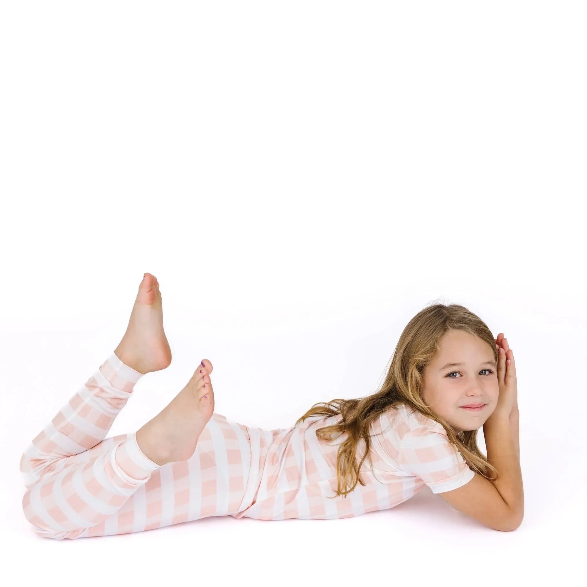 Girl in pink and white gingham pajamas lying on white background, cozy kids sleepwear