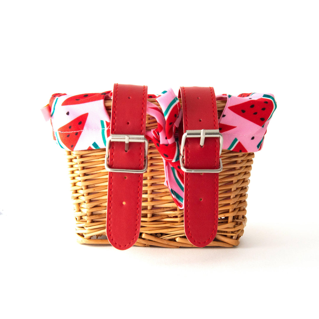 Woven bike basket with red straps and watermelon print liner, perfect for coastal adventures.