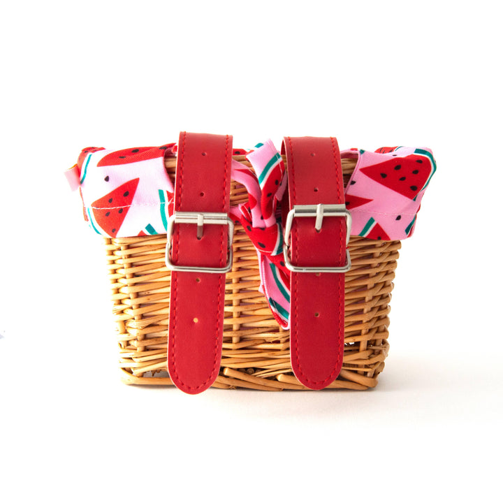 Woven bike basket with red straps and watermelon print liner, perfect for coastal adventures.