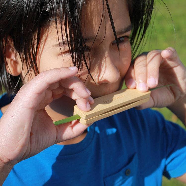 Child playing wooden harmonica outdoors, PNW adventure gear for kids