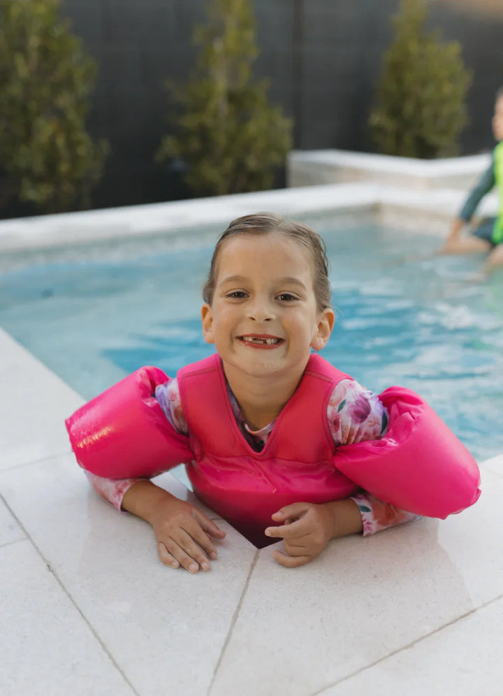 Child smiling in pink floaties at poolside, enjoying water safety gear for swimming fun