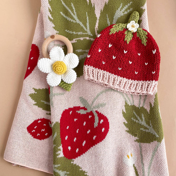 Strawberry knit hat and daisy teether on floral blanket, perfect for baby&