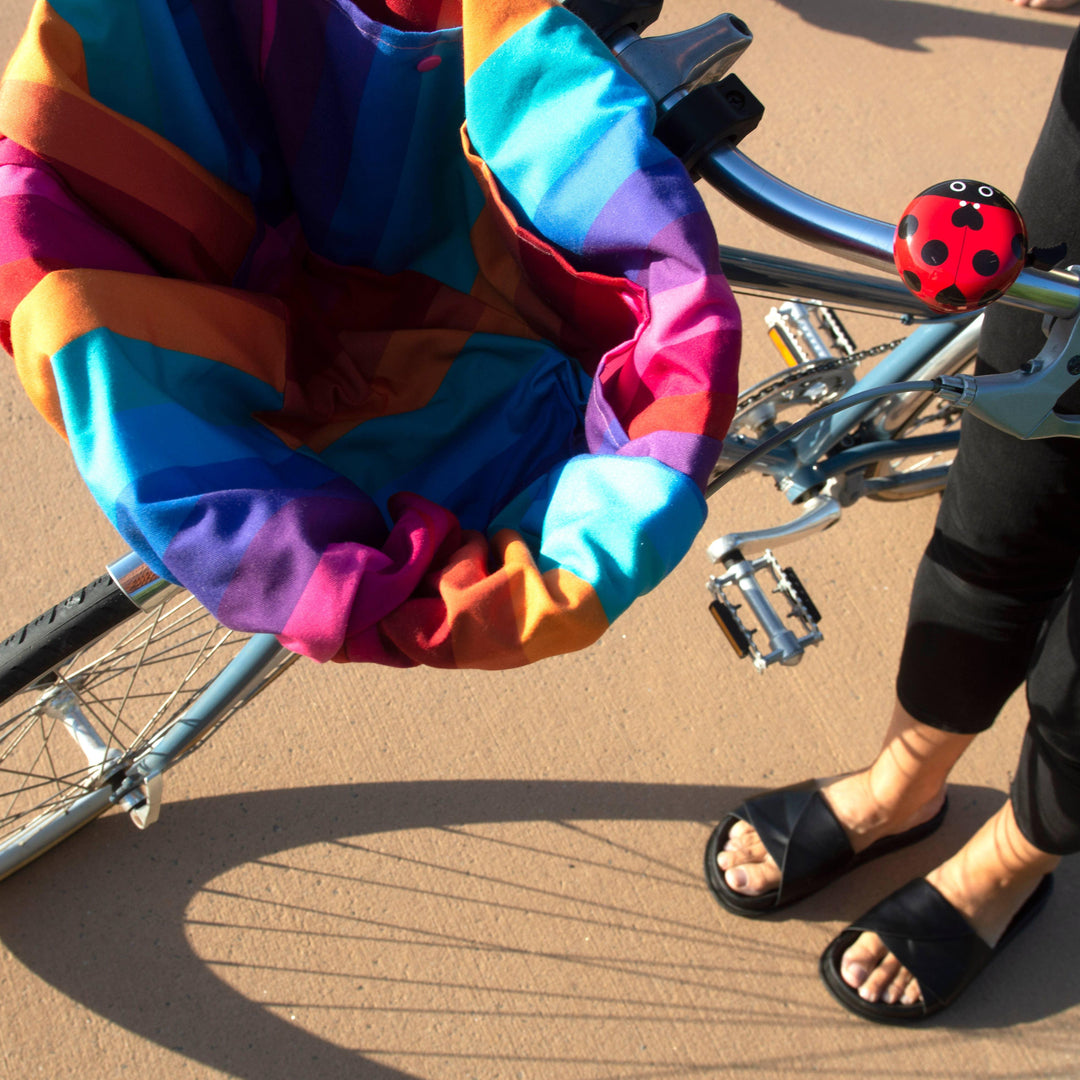 Colorful rainbow beach blanket on bike with ladybug bell, perfect for coastal adventures and bike rides.