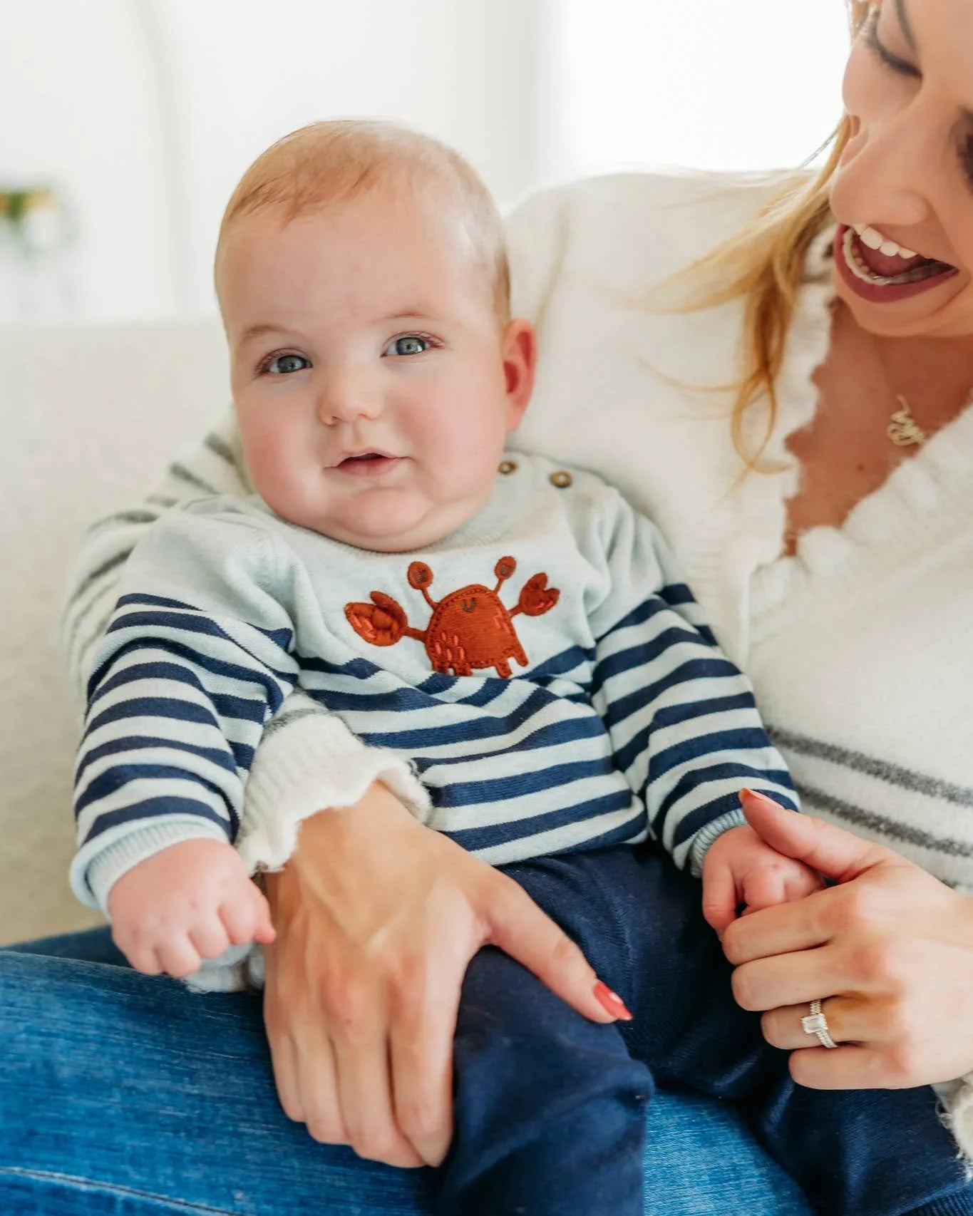 Baby in striped crab onesie held by smiling mom, cozy home setting