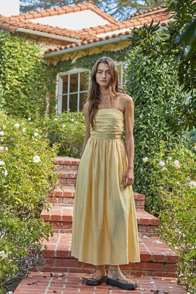 Woman in yellow striped strapless maxi dress on brick steps, coastal garden setting
