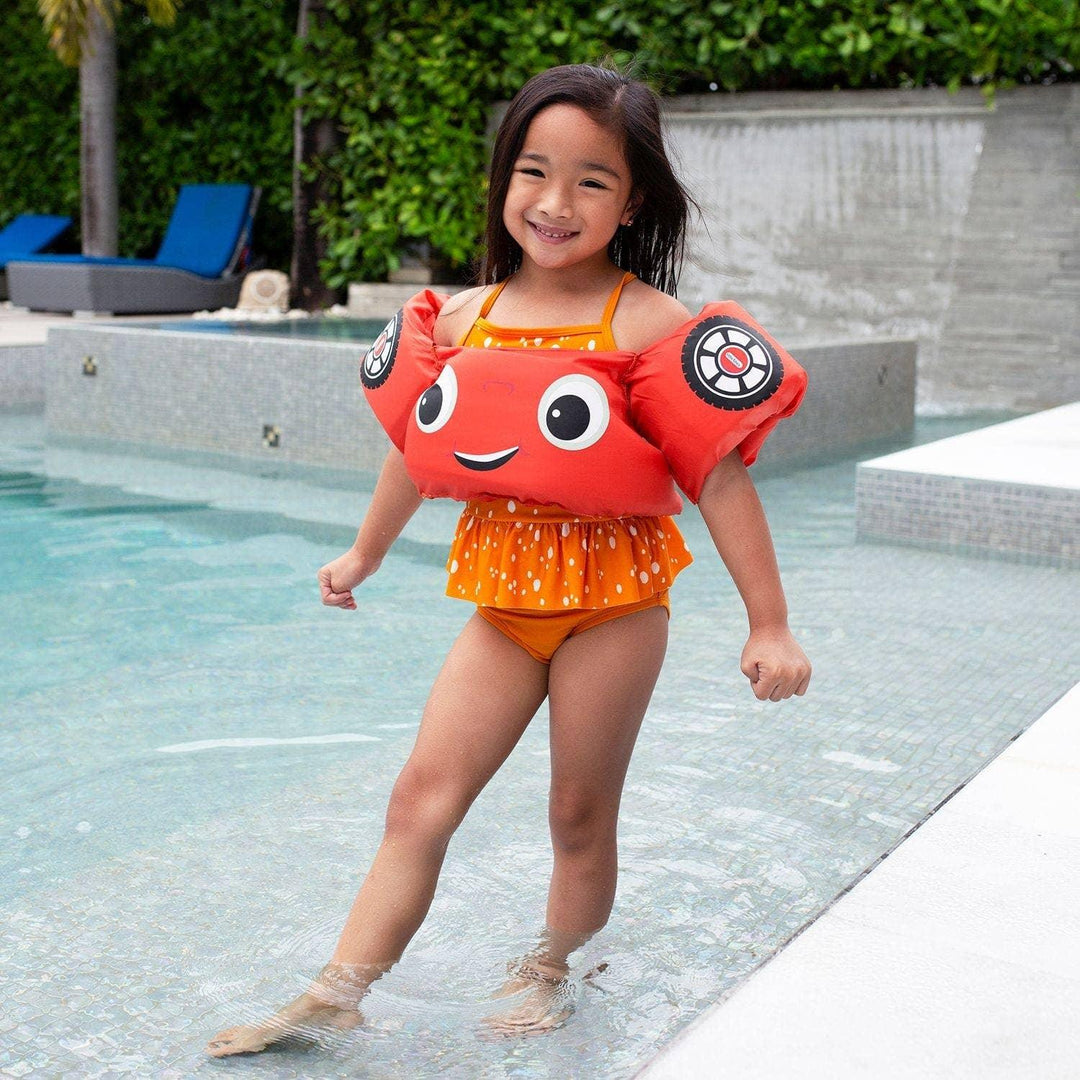 A young girl wearing a PoolCandy Cozy Coupe floatie vest in a swimming pool.