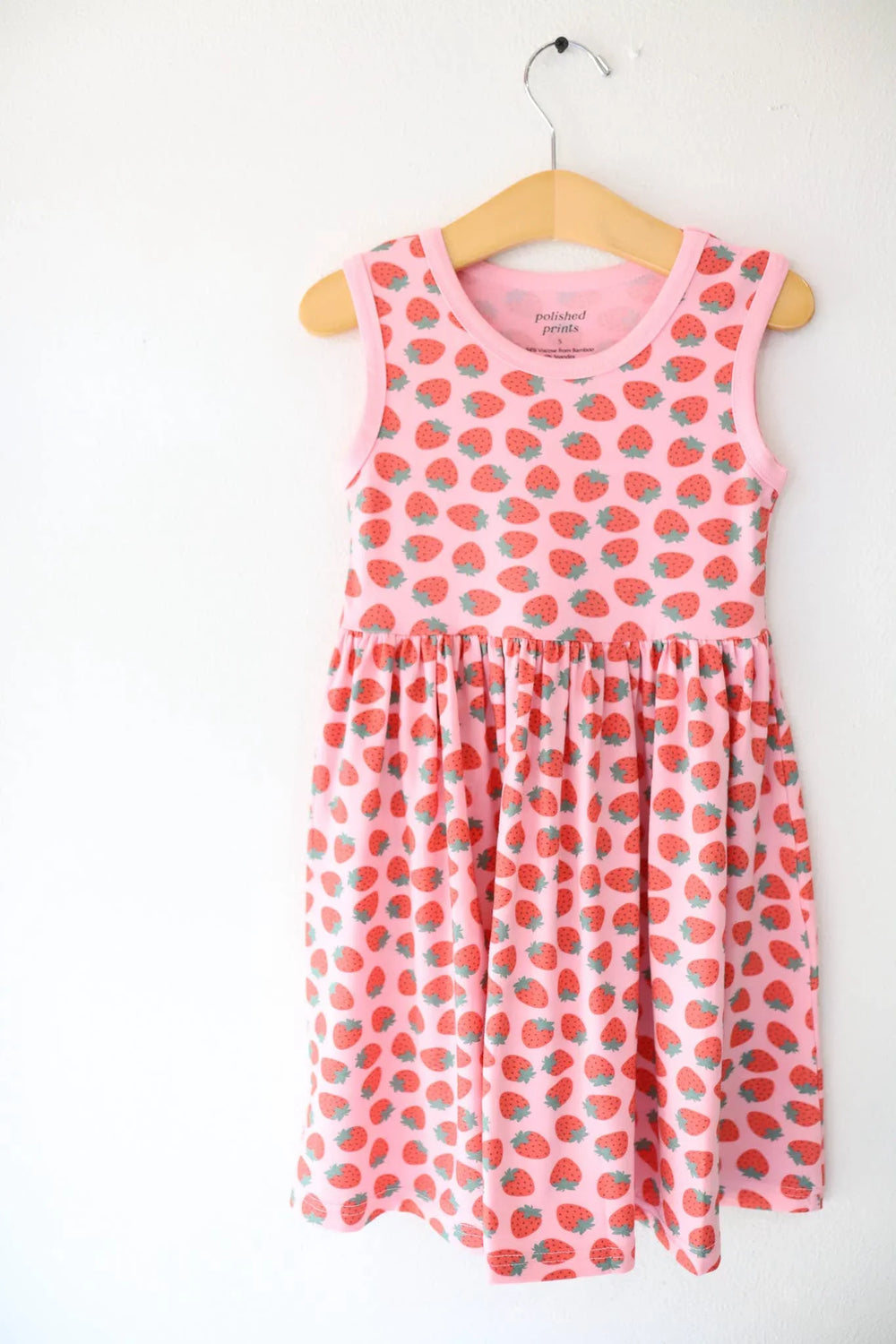 Pink strawberry print sleeveless kids dress on wooden hanger, perfect for beach days and coastal adventures