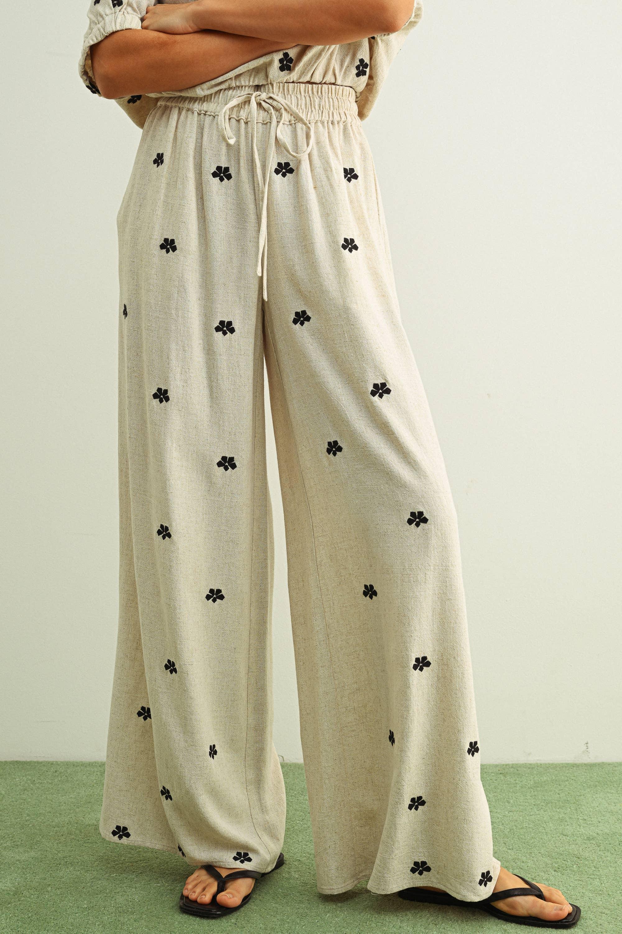 Beige wide-leg pants with black floral print, drawstring waist, paired with flip flops
