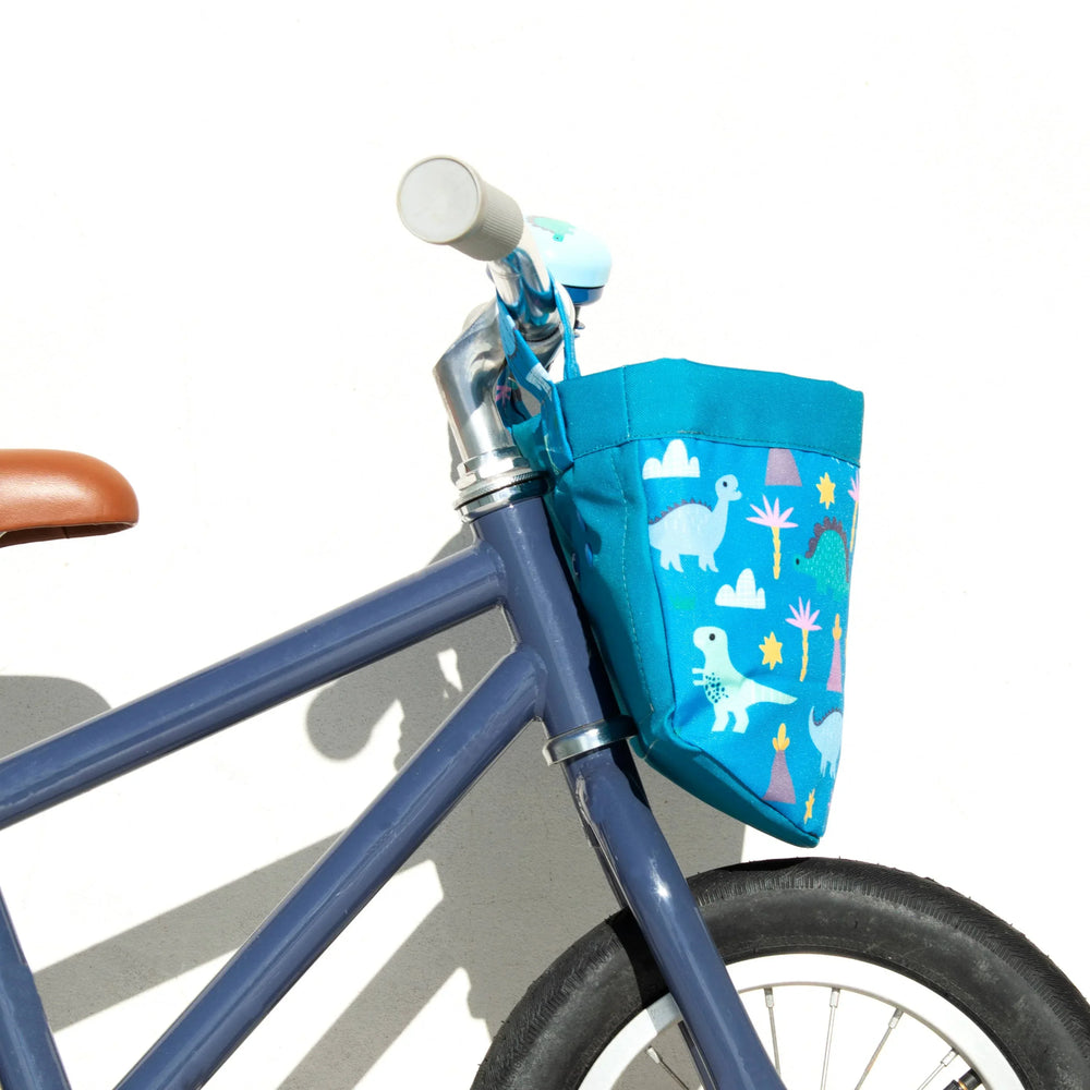 Blue kids bike with dinosaur print handlebar bag, perfect for coastal adventures and everyday rides.