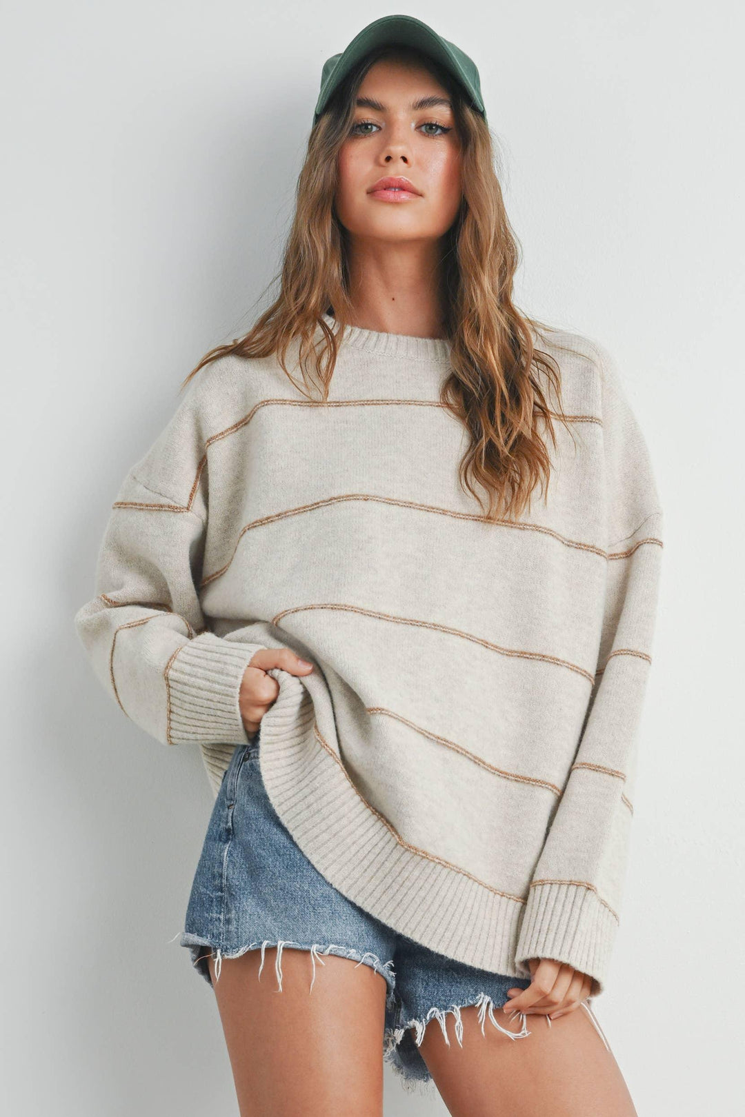 Woman in cozy striped sweater, denim shorts, and green cap for casual outdoor style