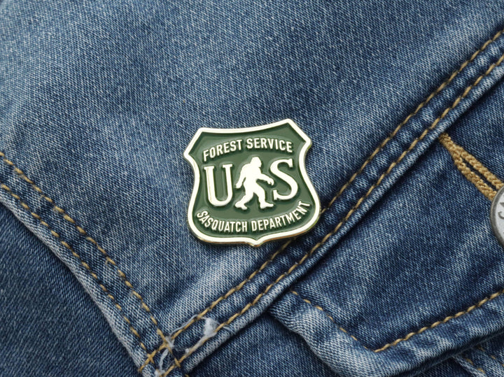Forest Service Sasquatch Department enamel pin on denim, outdoor adventure accessory