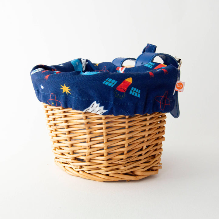 Wicker bike basket with space-themed navy liner, rockets, stars, and BEEP tag for outdoor adventures.