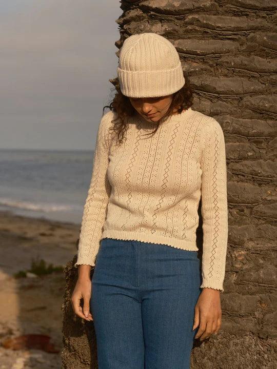 Cream knit sweater with diamond pattern, beanie, and jeans by beach for coastal PNW style