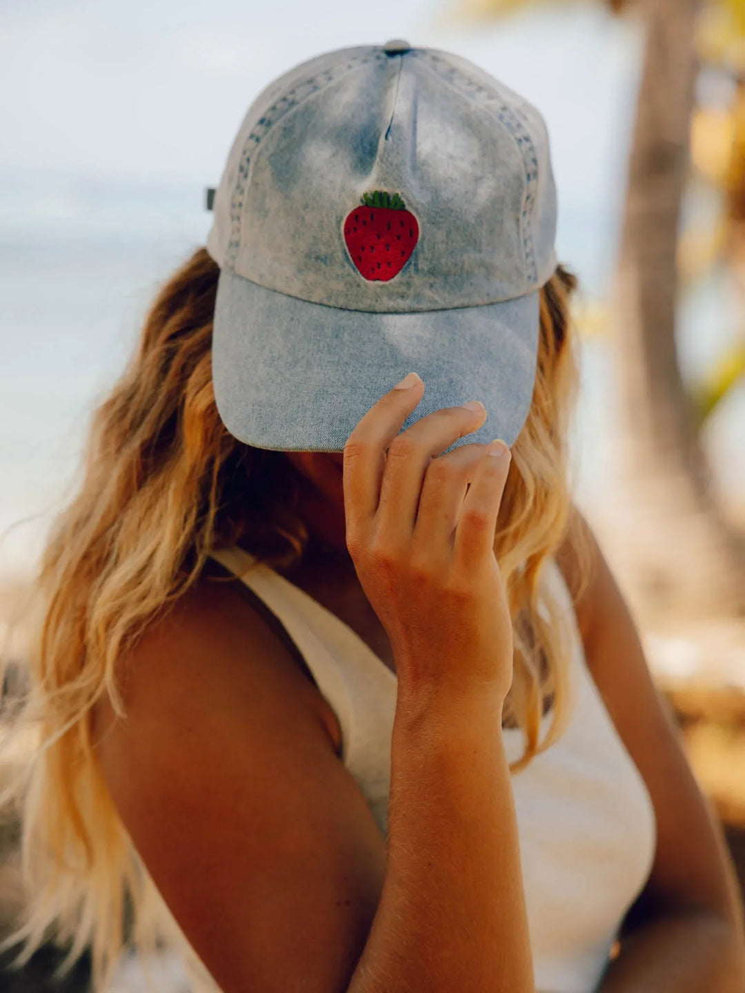 Woman wearing denim baseball cap with embroidered strawberry, beach style outdoor gear